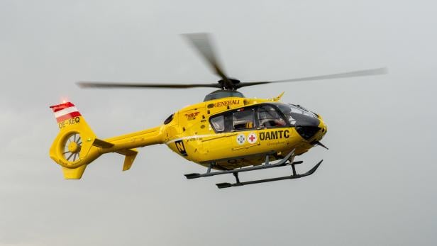 Ein gelber Christophorus Hubschrauber des ÖAMTC fliegt am grauen Himmel.