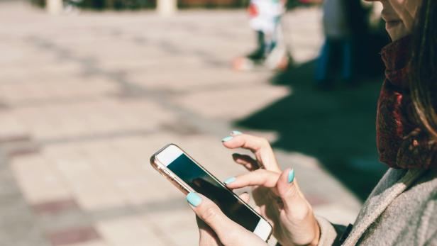 Frau mit türkisen Fingernägeln hält ein Handy in der Hand