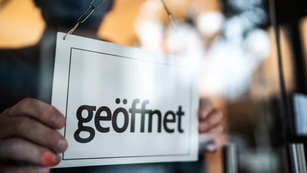 Business ower holding open sign (geöffnet) on storefront door