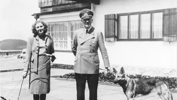 Eva Braun und Adolf Hitler mit Schäferhündin stehen auf der Terrasse des Berghofs.