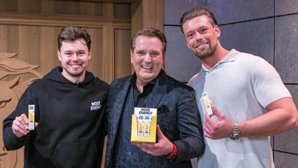 Drei Männer, zwei in schwarz gekleidet und ein Mann in einem grauen T-Shirt, halten ein Produkt in die Kamera